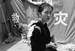 8月6日，一位受灾群众背着孩子从鲁甸县龙头山镇的临时安置点的帐篷旁走过。
